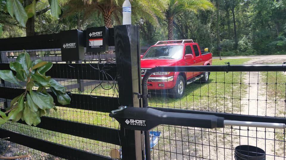 Red truck entering a black gate, controlled by an automatic gate opener in a green outdoor setting.