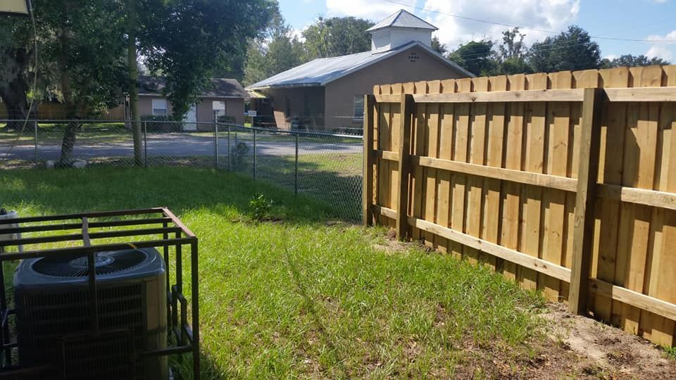 Backyard with a wooden fence, chain-link fence, air conditioner unit, and a house in the background.