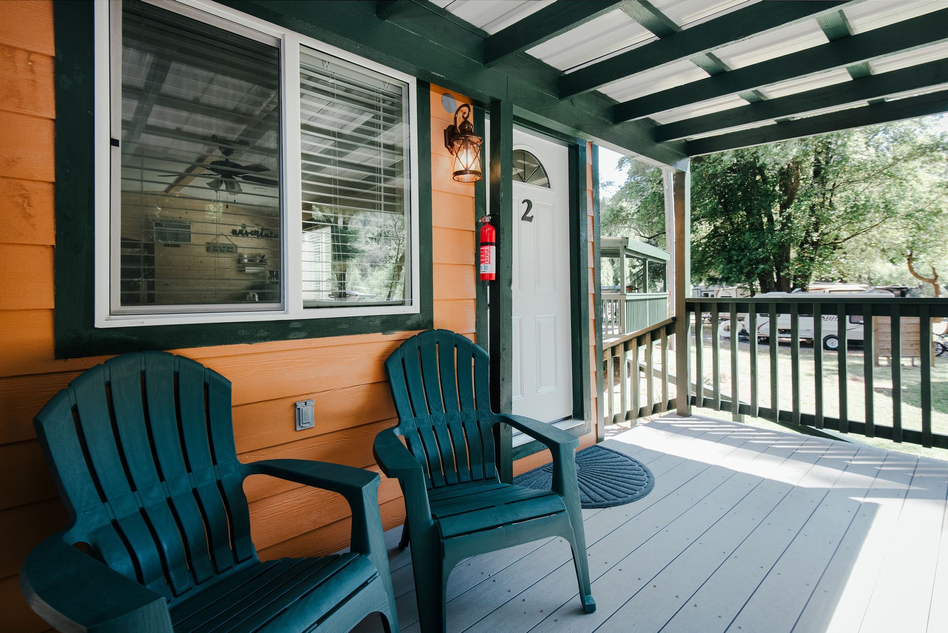 Two teal chairs sit on a covered wooden porch next to a white door labeled 