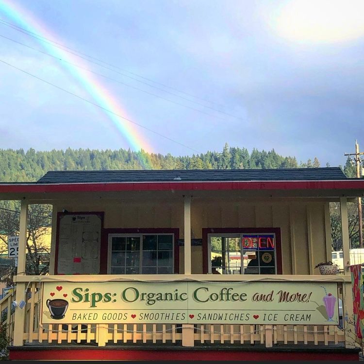 A white cup of espresso on a saucer, surrounded by scattered dark coffee beans and a burlap sack on a wooden table.