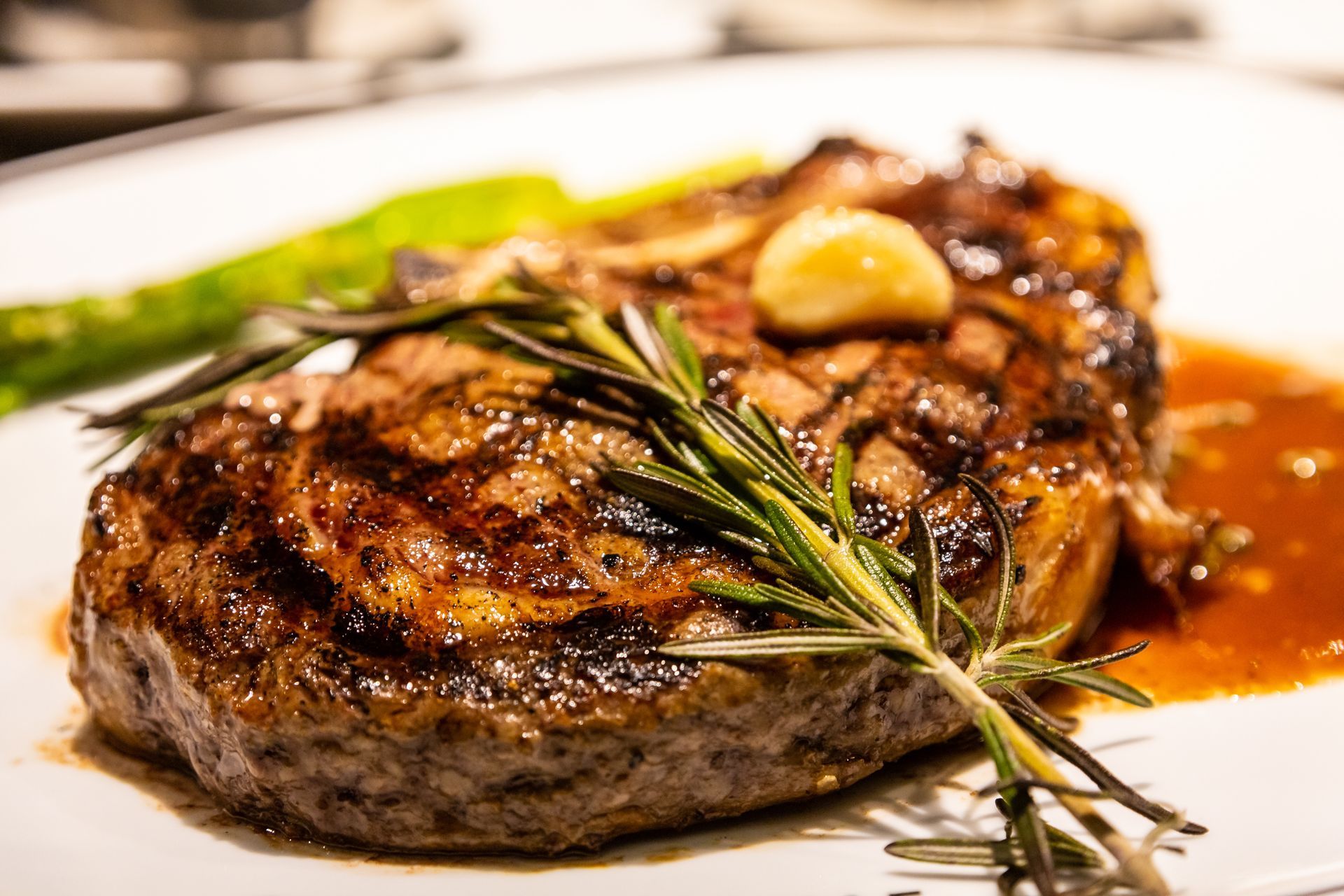 A grilled steak topped with a clove of garlic and a sprig of rosemary, served with sauce on a white plate.