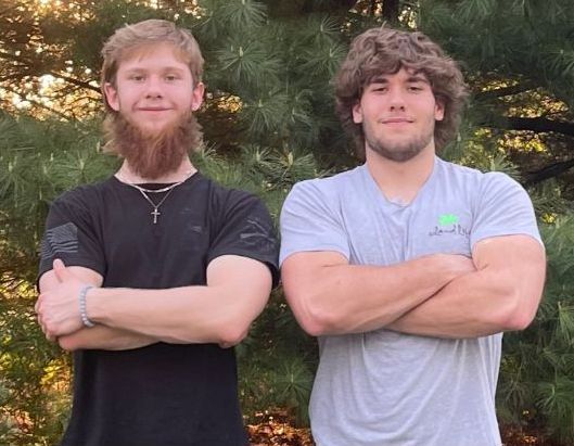 Two men are posing for a picture in front of a christmas tree.