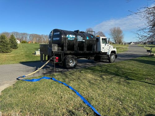 A tanker truck is parked in a grassy field with a blue hose attached to it.