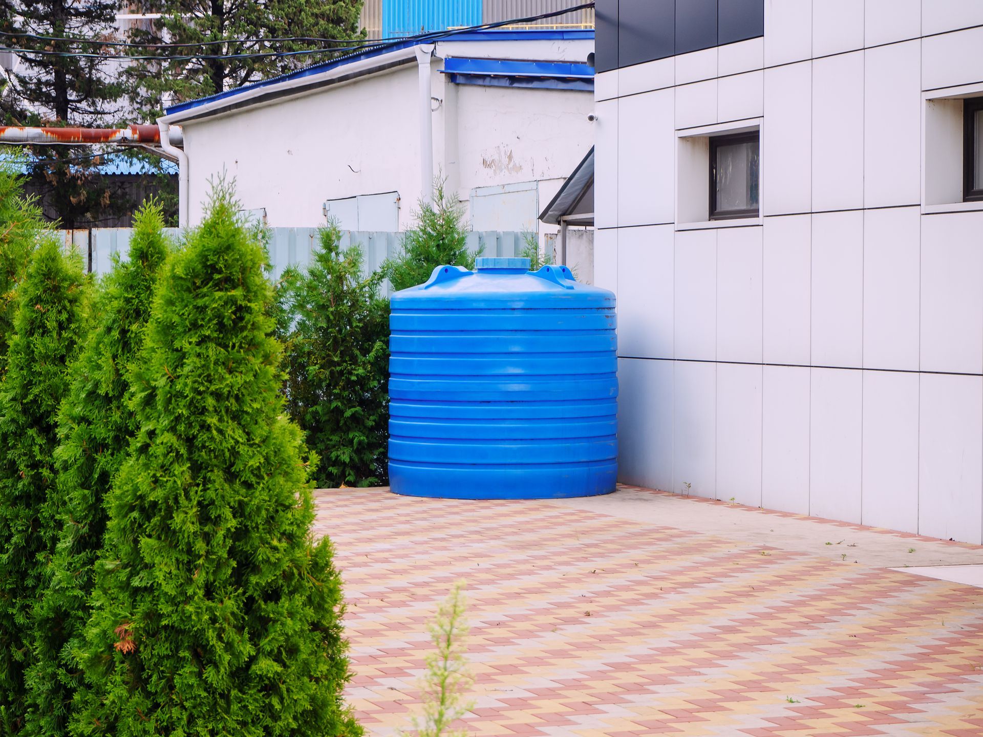 A blue water tank is sitting on the sidewalk in front of a building.