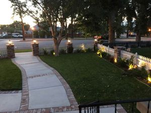 A brick walkway leading to a white picket fence