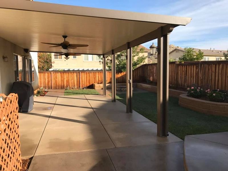 A patio with a ceiling fan and a wooden fence in the background.