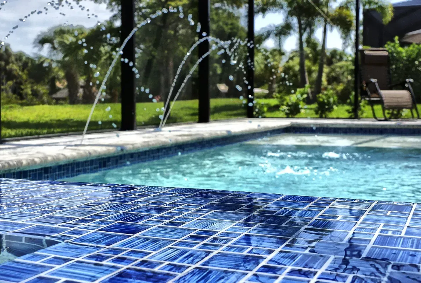Blue-tiled pool with a fountain, lush green yard in the background.