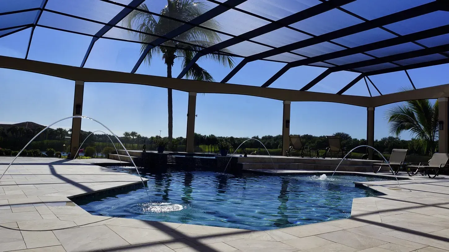 Swimming pool under a screened enclosure with water fountains. Blue water and sunny sky.