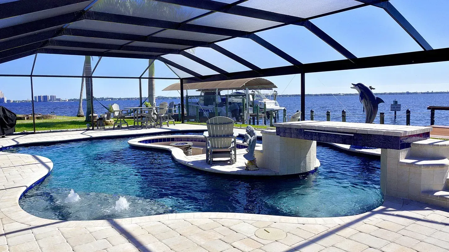 Pool with water features, island, and dolphin statue, overlooking a waterfront with cityscape.