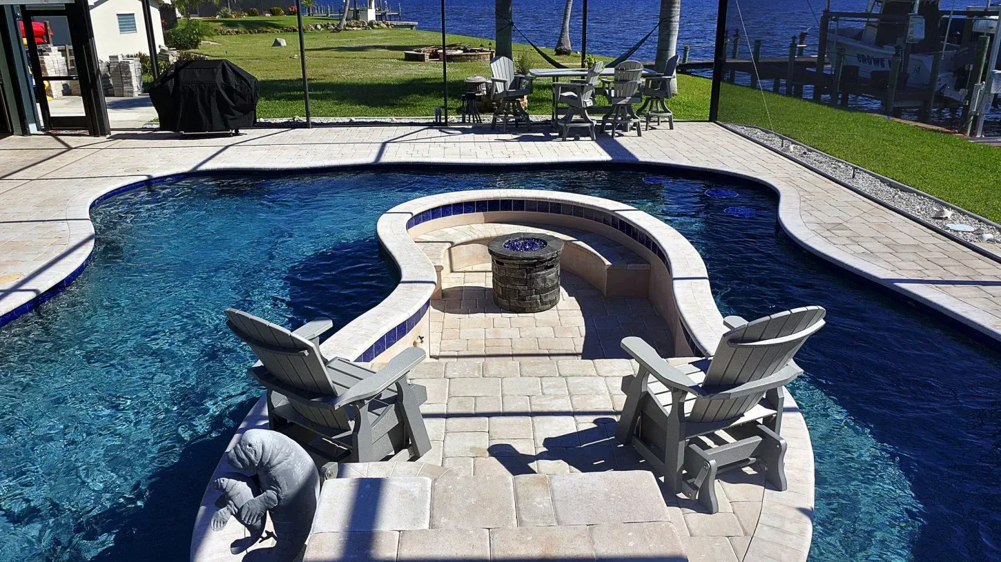 Poolside area with Adirondack chairs, a fire pit, and water view.