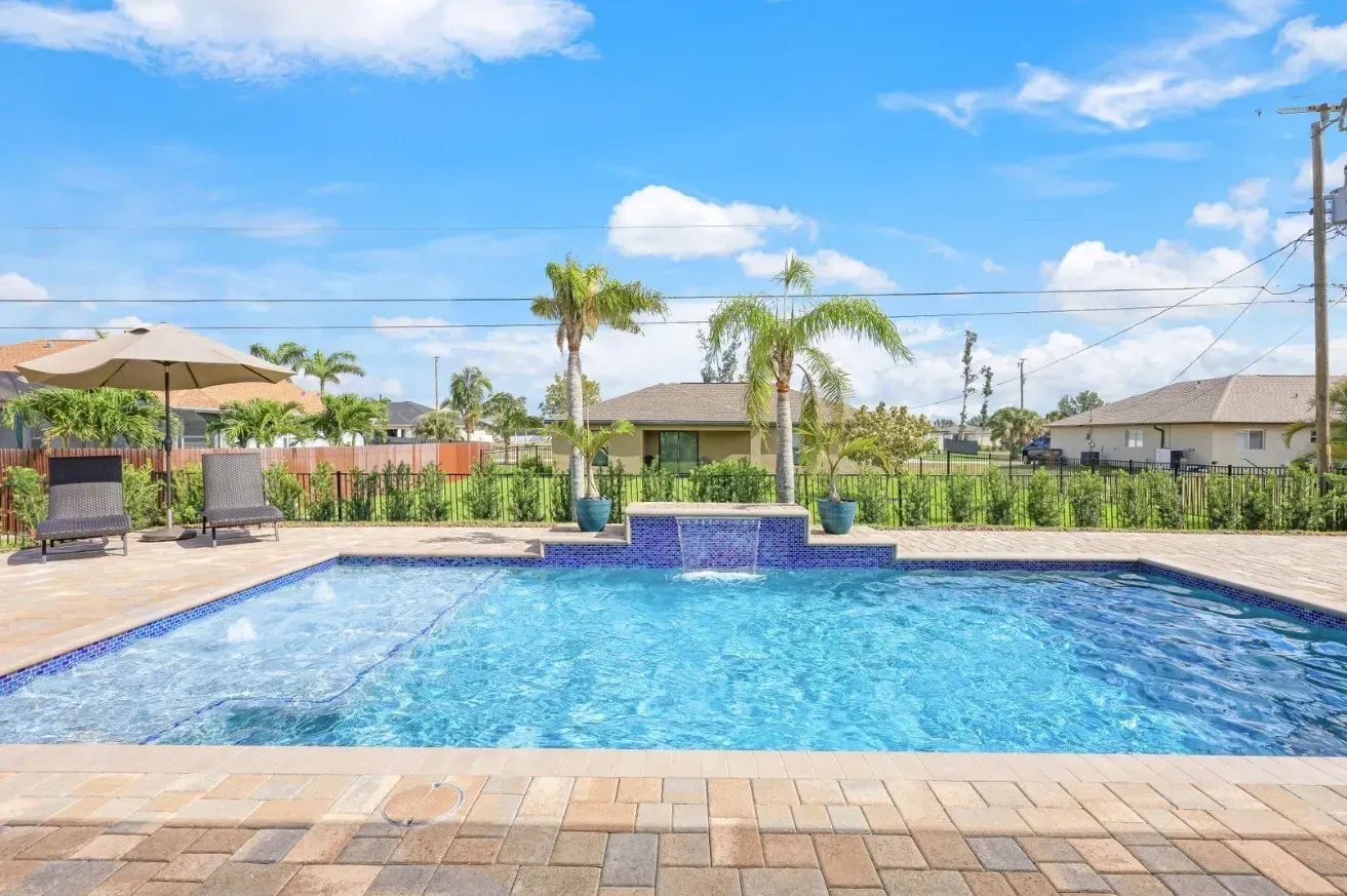 Swimming pool with blue tile, waterfall, palm trees, and blue sky.