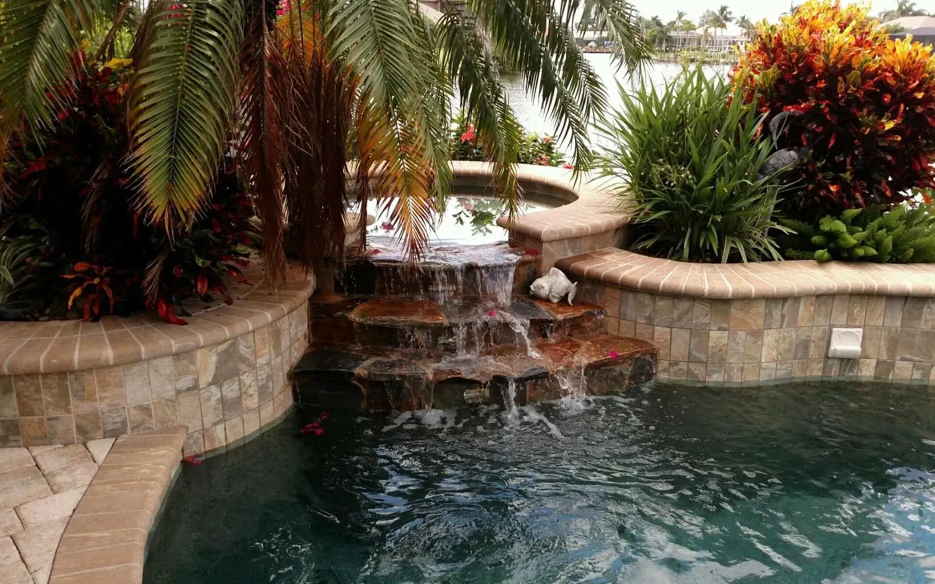 Waterfall cascading into a pool, surrounded by lush plants and stone borders.