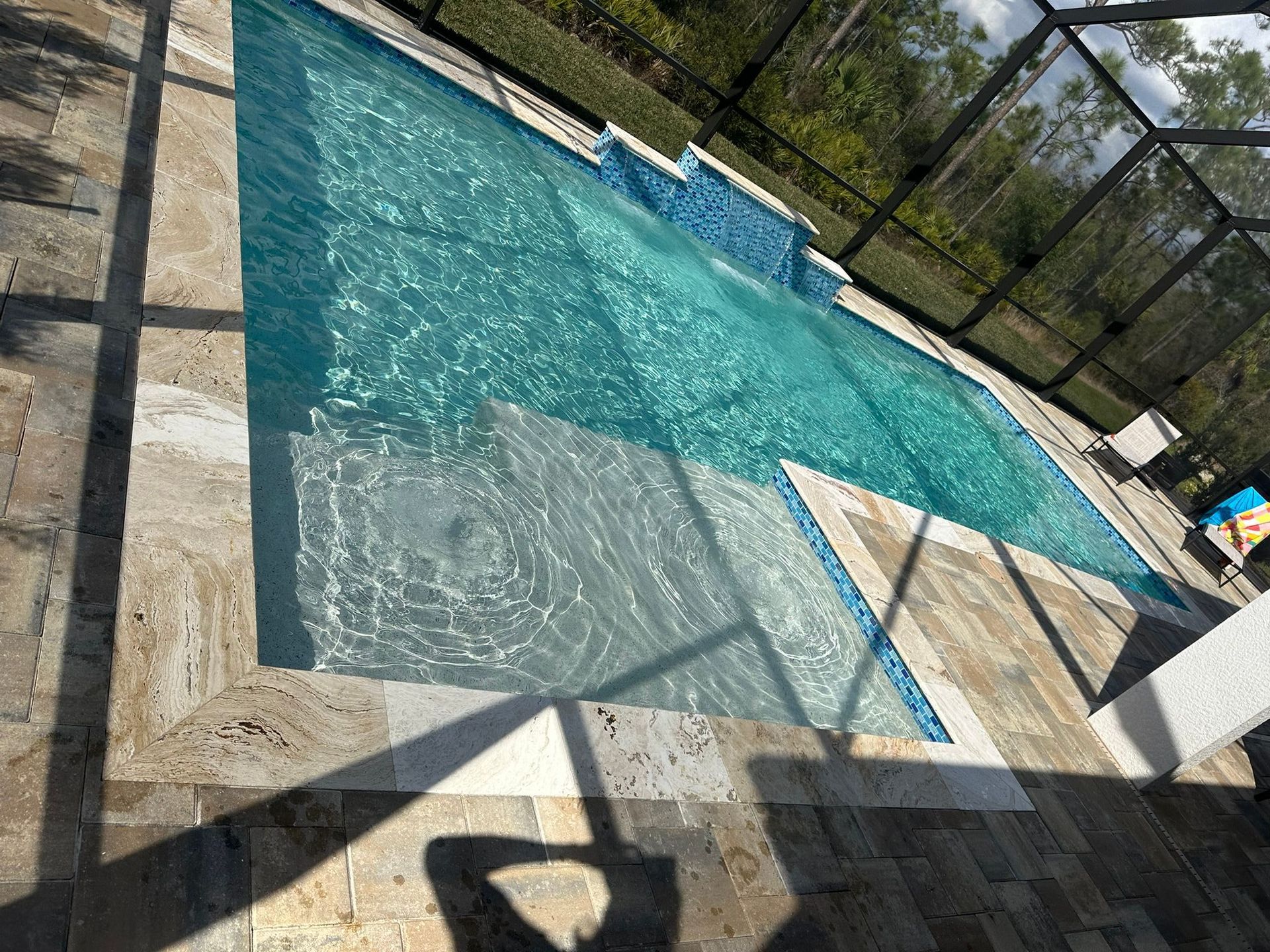 Pool with clear blue water, tan tile surround, and blue tile accents; outdoors.