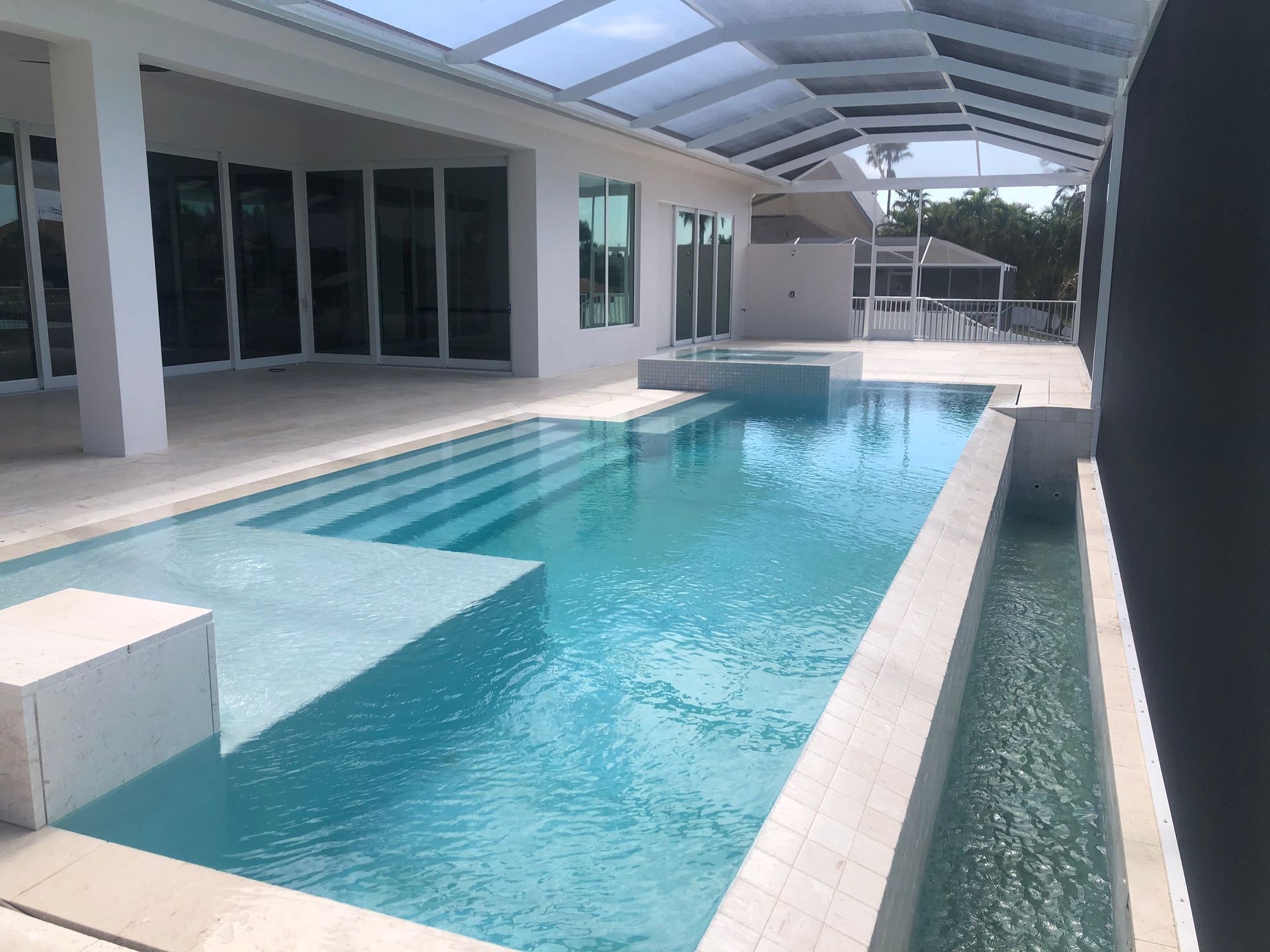 Poolside view: light blue pool with steps, white patio, and covered lanai.