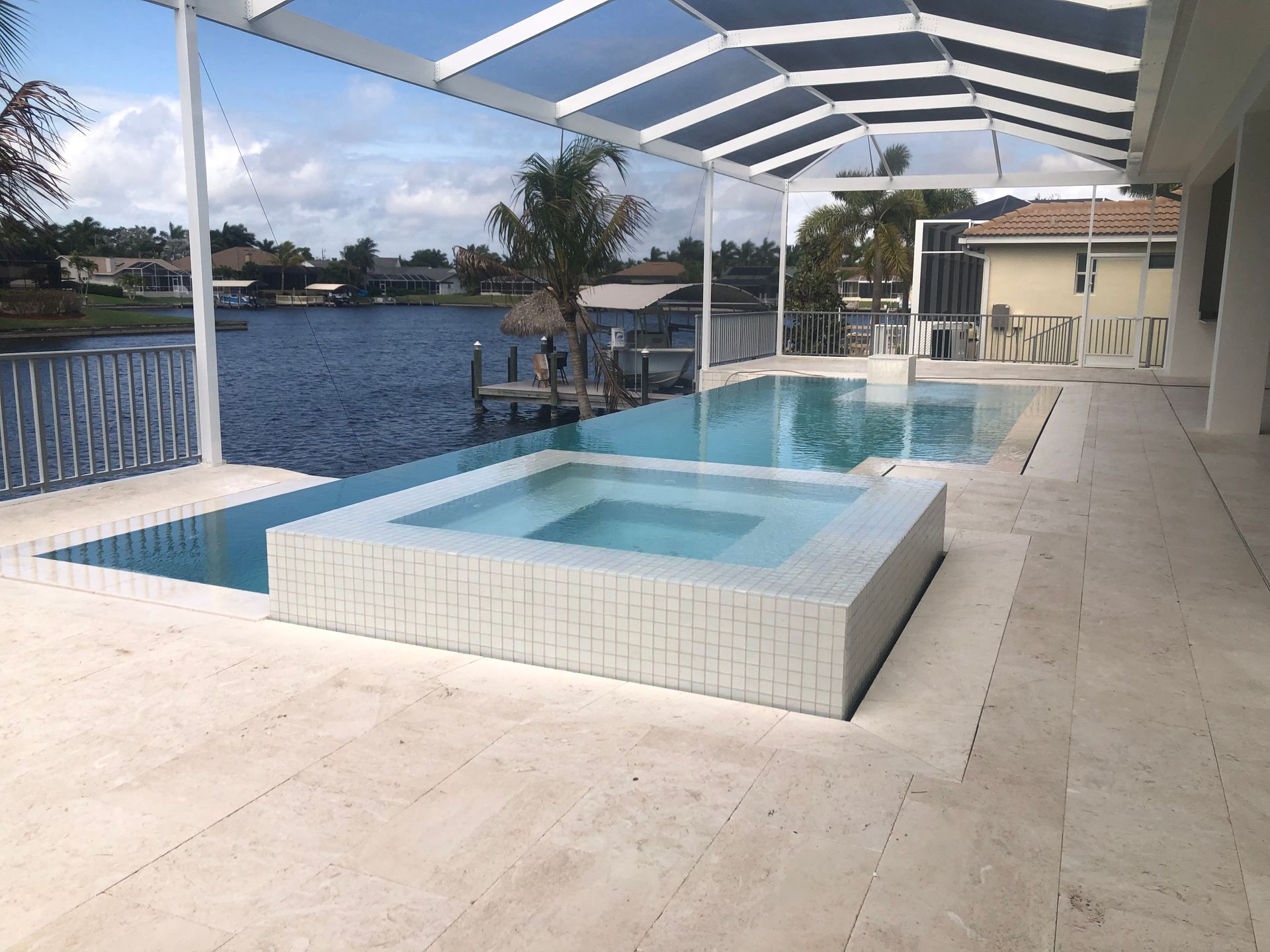 Pool and spa with a view of a waterway, screened patio, light-colored tiles, and blue water.