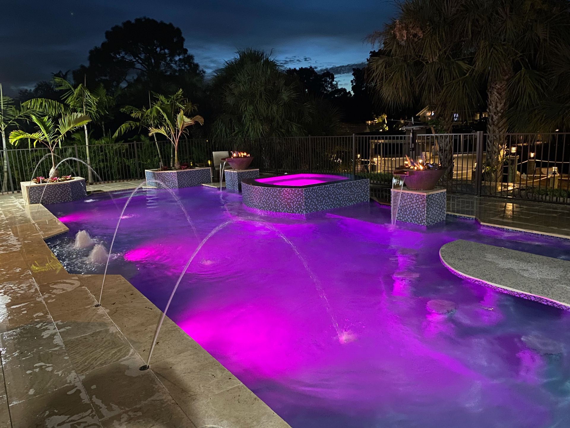 Nighttime illuminated pool with purple lighting and fountains.