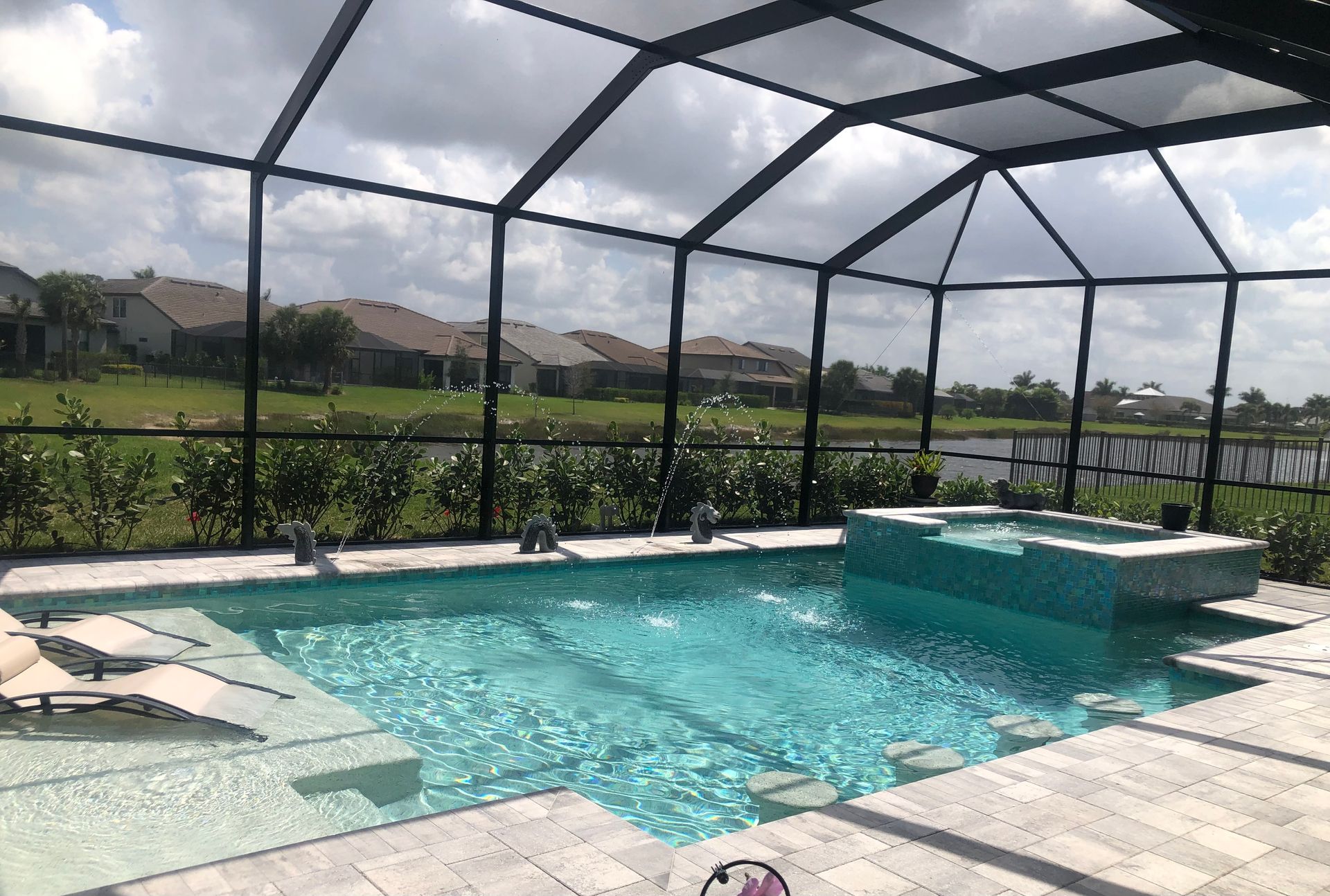 Pool area with turquoise water, jacuzzi, and screened enclosure under a cloudy sky.