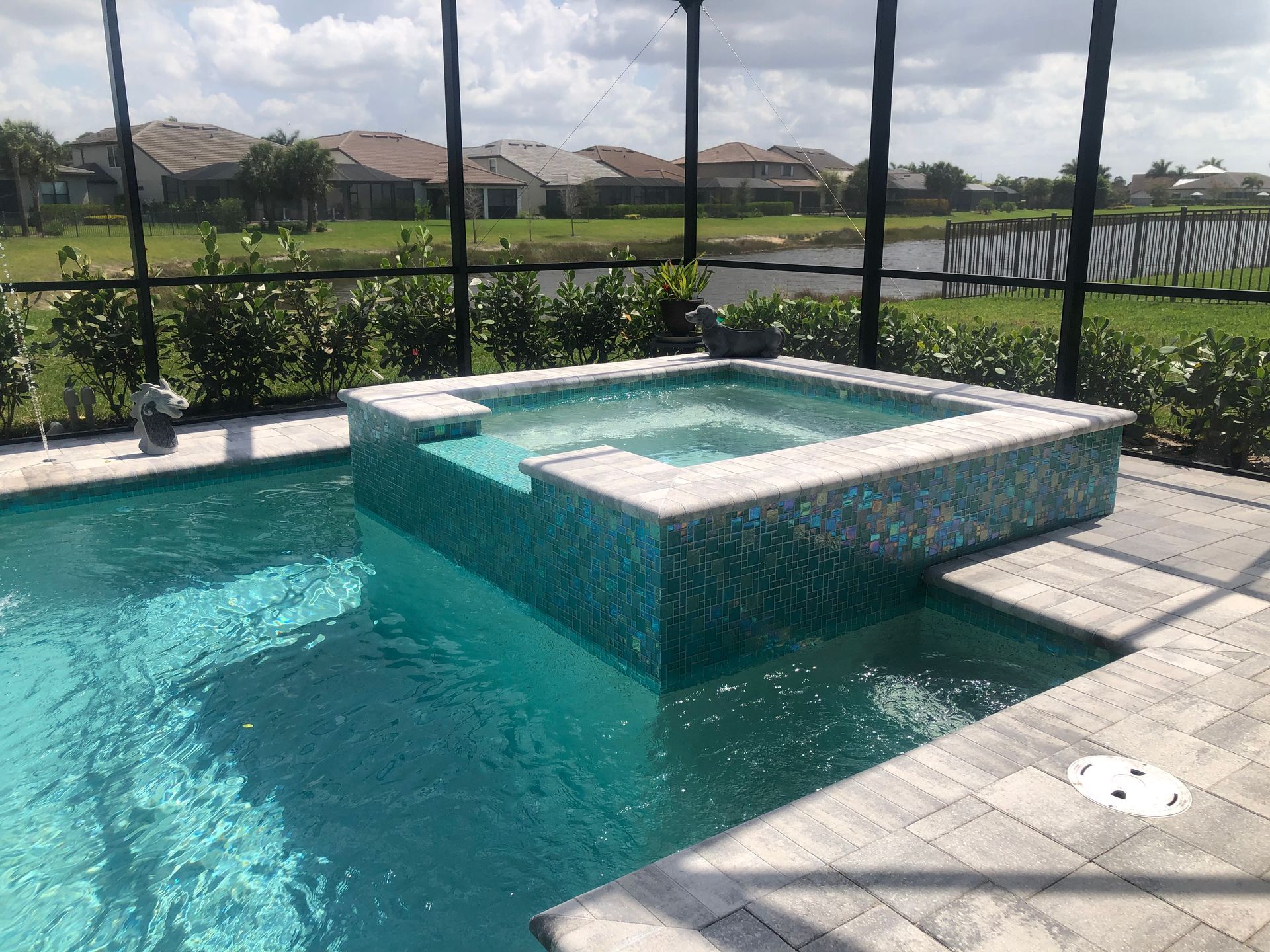 Swimming pool with raised spa, blue tile, and brick patio. Houses and screen enclosure in the background.
