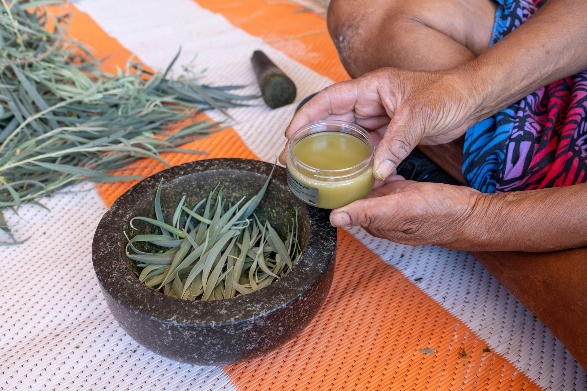 A person is holding a jar of liquid next to a mortar and pestle.