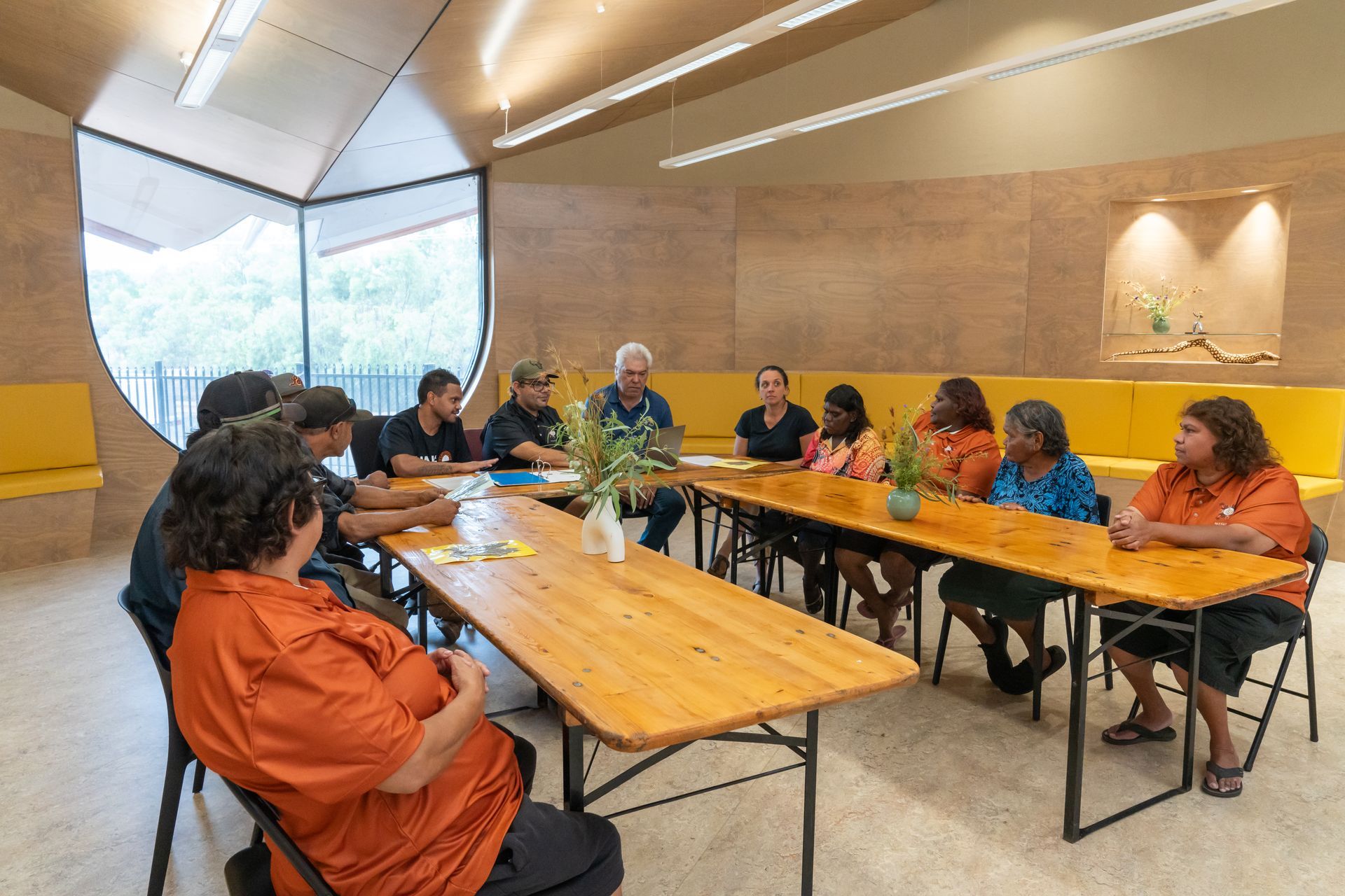 A group of people are sitting around a long wooden table in a room.