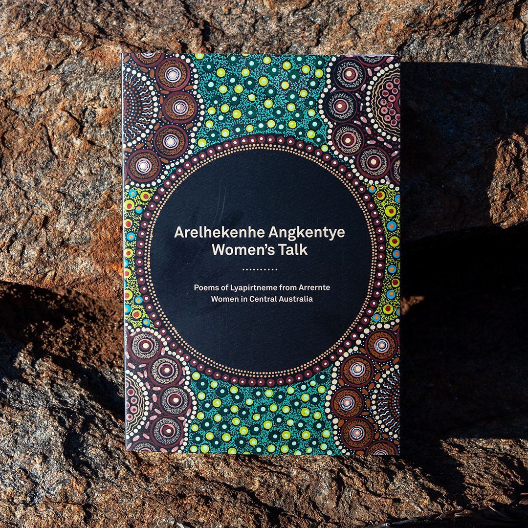 A book titled arelhkenha angkentyn women 's talk is sitting on a rock.