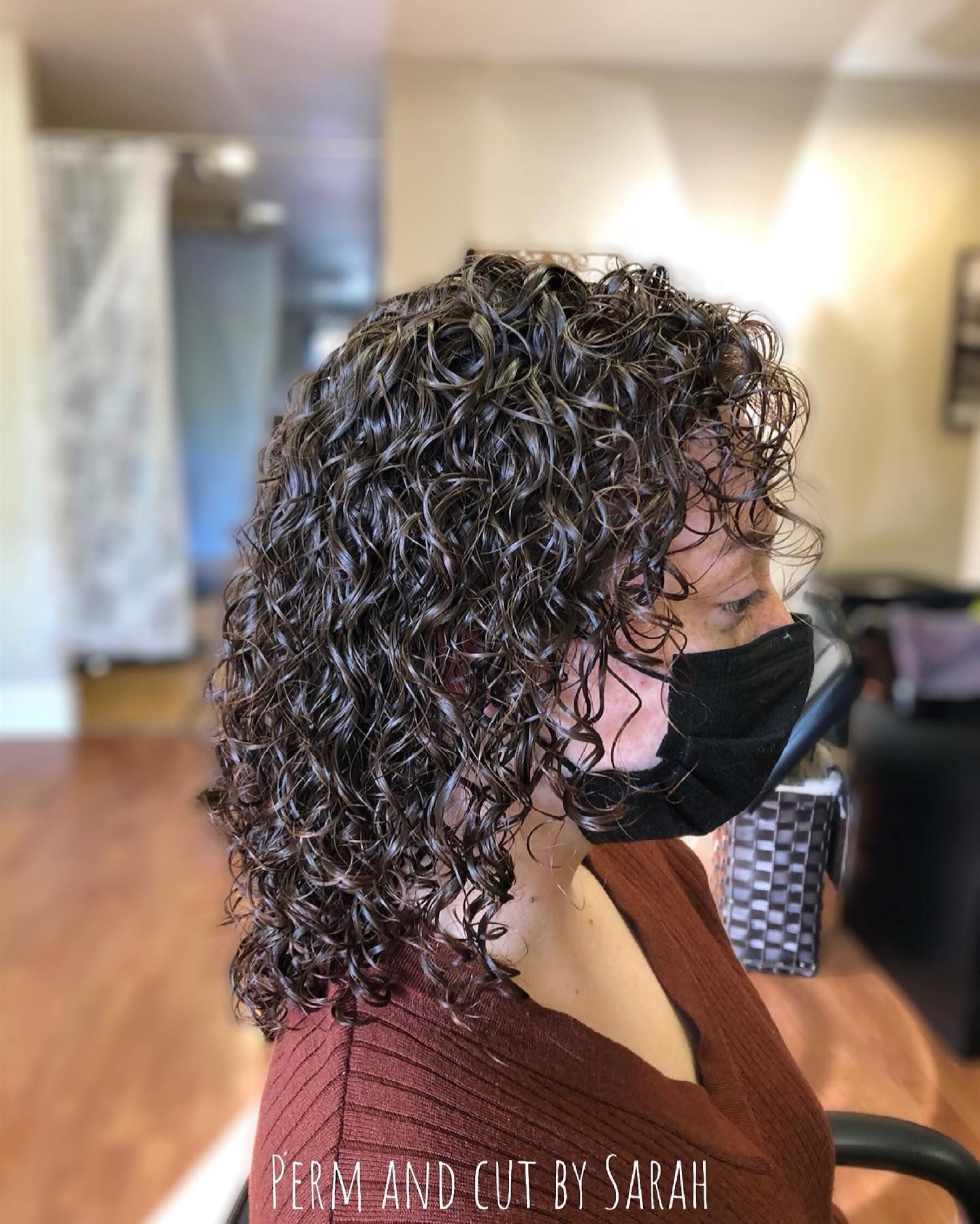 Side-profile of a person with curly dark hair wearing a black mask in a salon chair