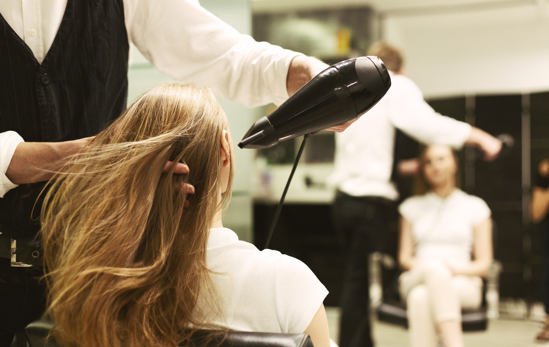 Hairdresser blow-drying a client’s long hair in a salon