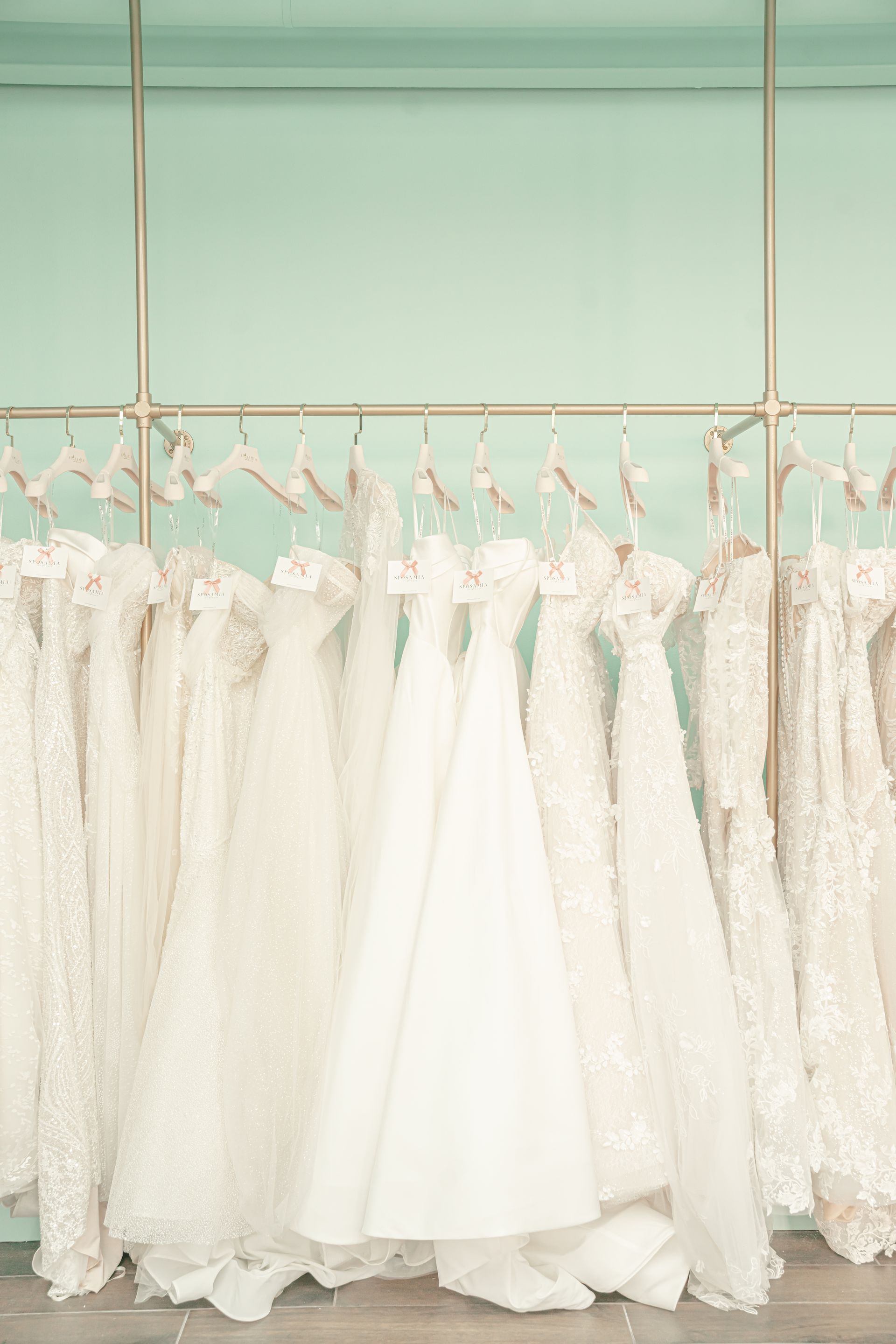 A row of white wedding dresses hanging on a rack in a store.