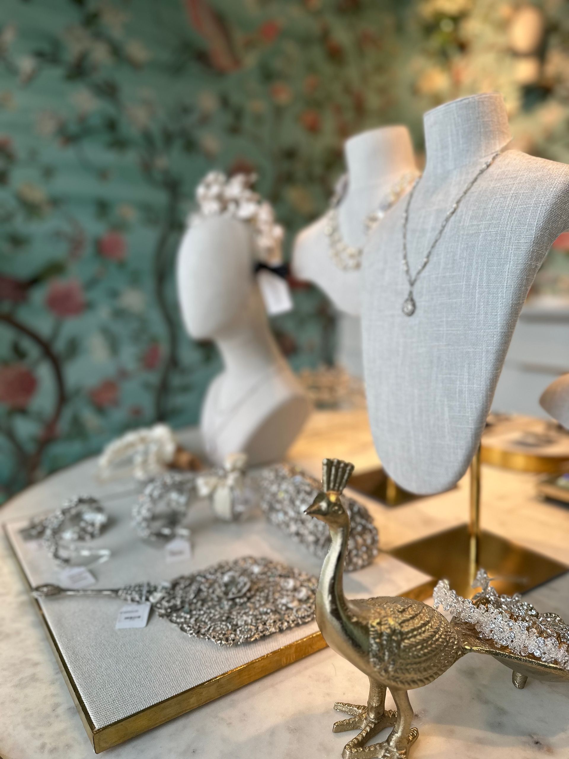 A peacock is sitting on a table next to a mannequin displaying jewelry.