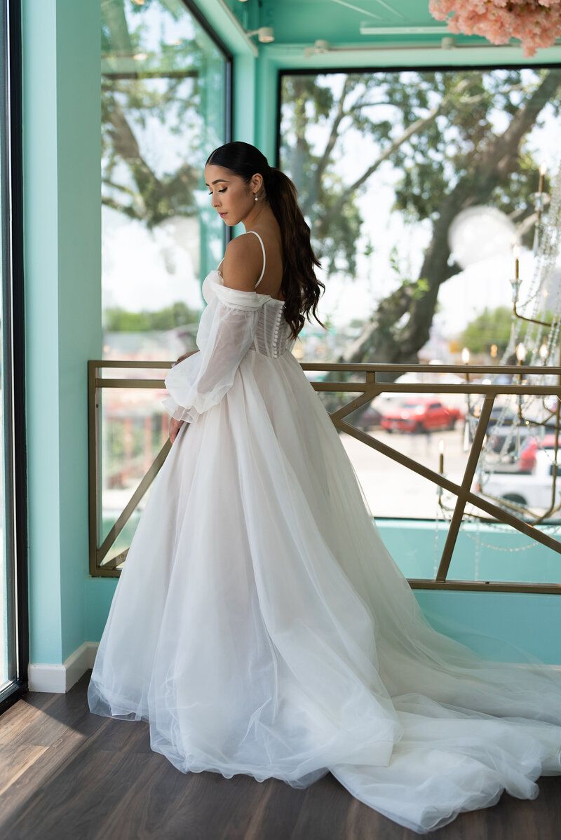 A woman in a white wedding dress is standing in front of a window.