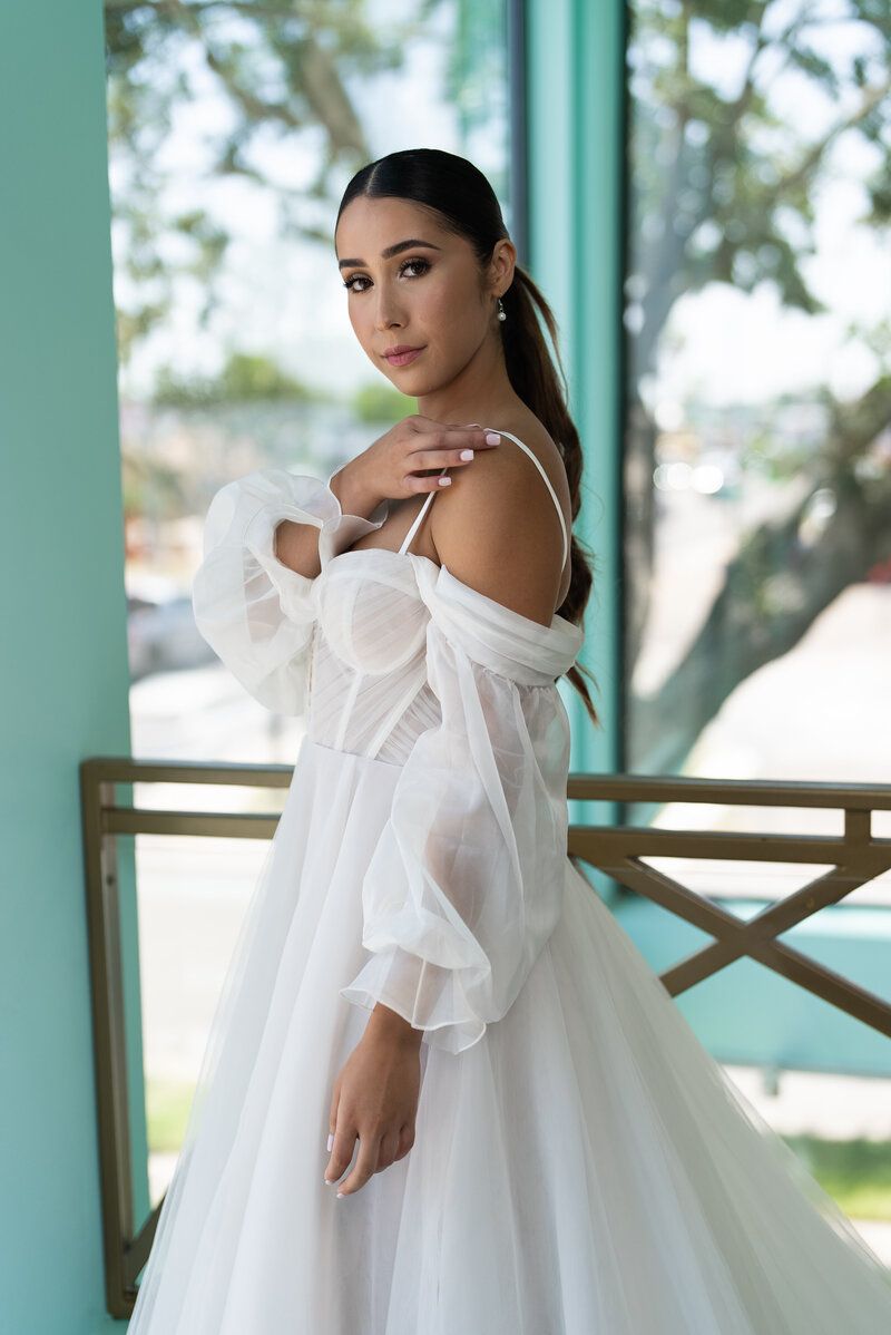 A woman in a white dress is standing in front of a window.