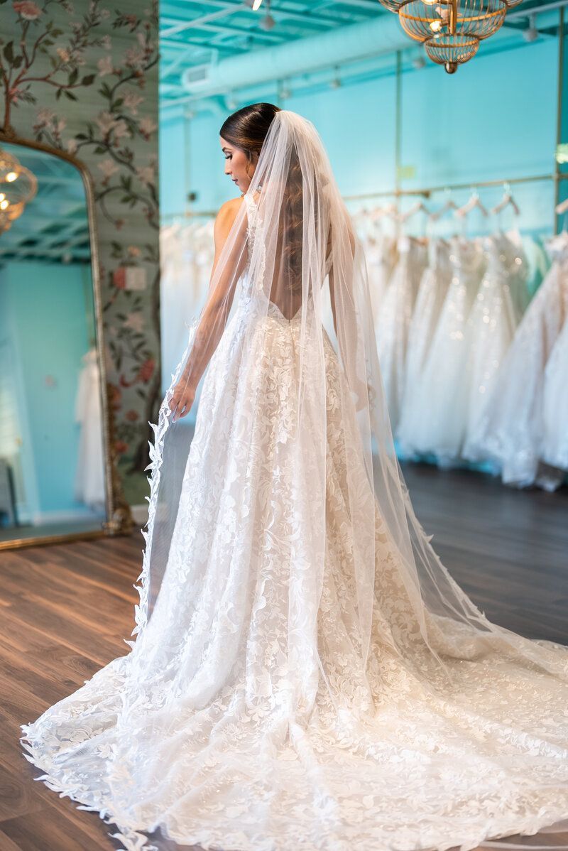 A woman in a wedding dress and veil is standing in front of a mirror.