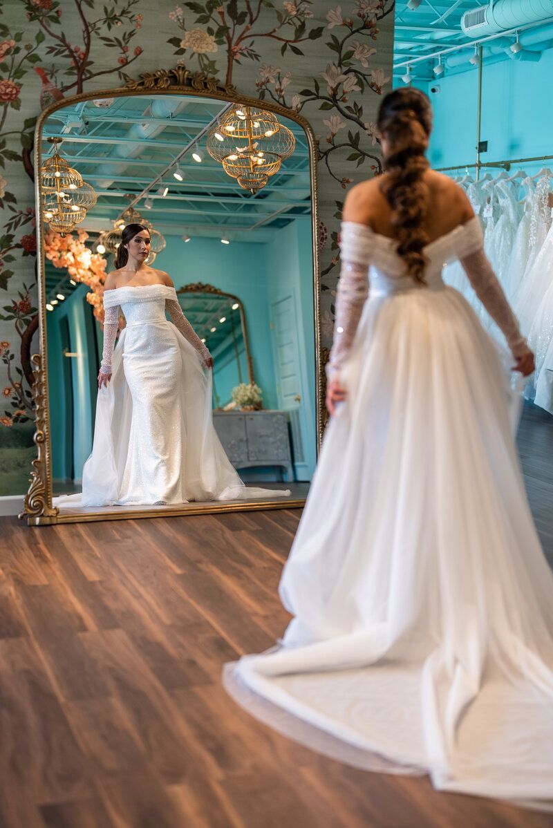 A woman in a wedding dress is standing in front of a large mirror.