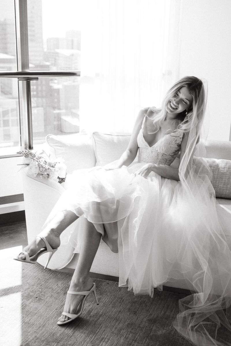 A woman in a wedding dress is sitting on a couch in front of a window.