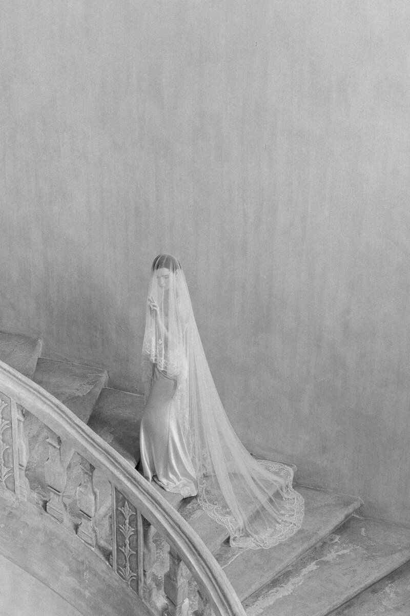 A woman in a wedding dress and veil is walking down a set of stairs.