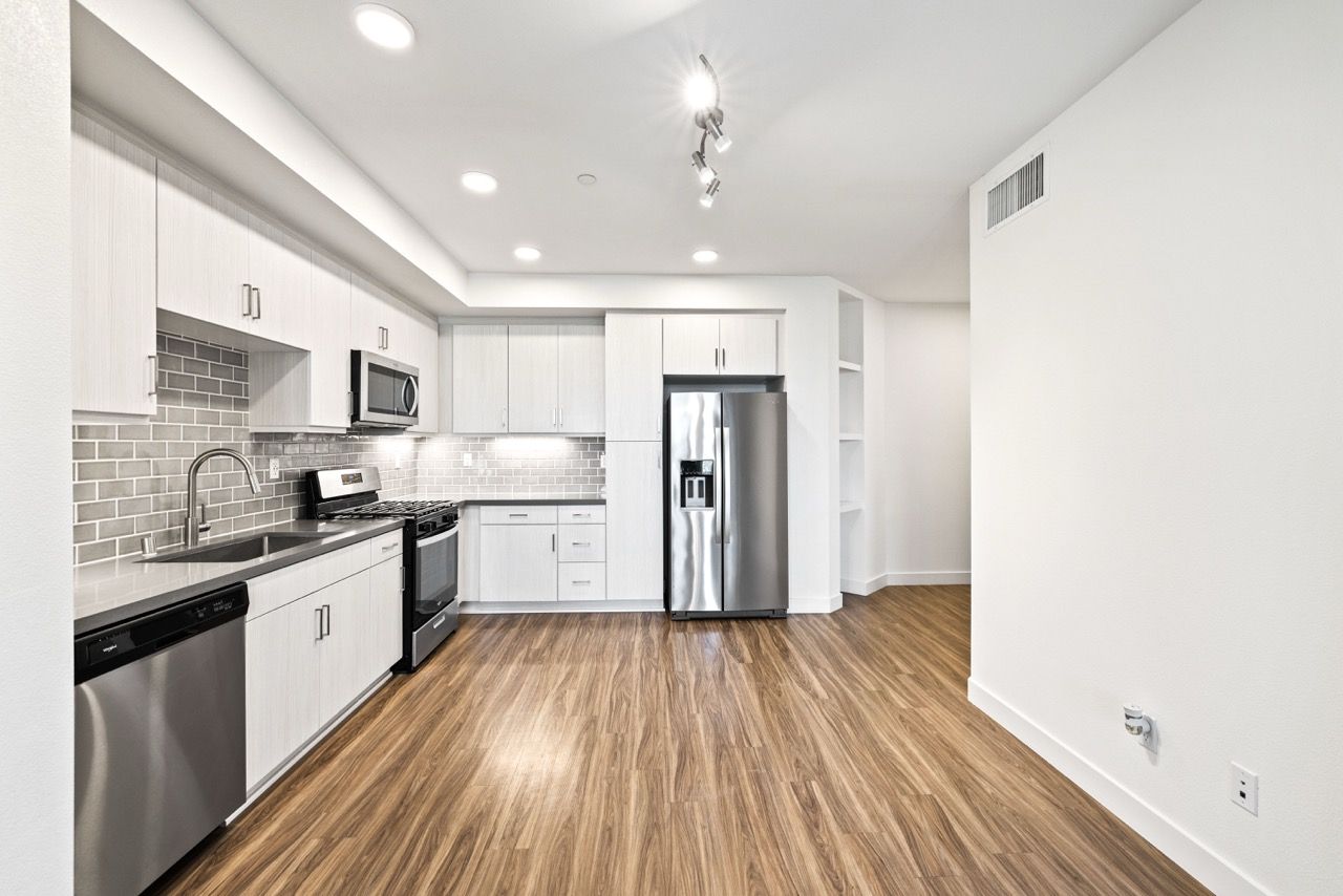 Modern kitchen in an apartment with stainless steel appliances, white cabinets, and wood-look flooring.