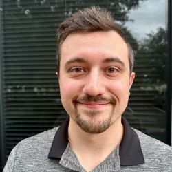 A man with a beard is smiling for the camera in front of a window.