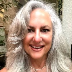 A woman with gray hair is smiling and wearing a necklace.