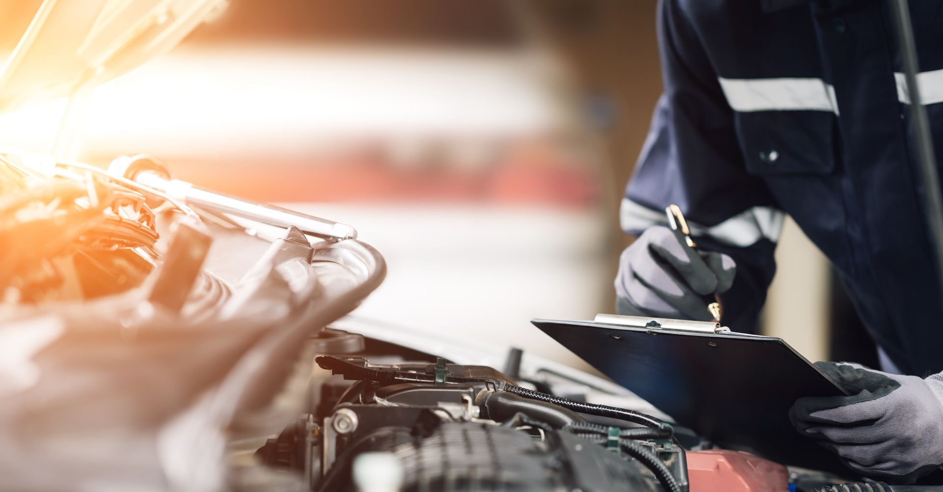 Mechanic in blue jumpsuit checks car engine with clipboard and pen in a garage setting.