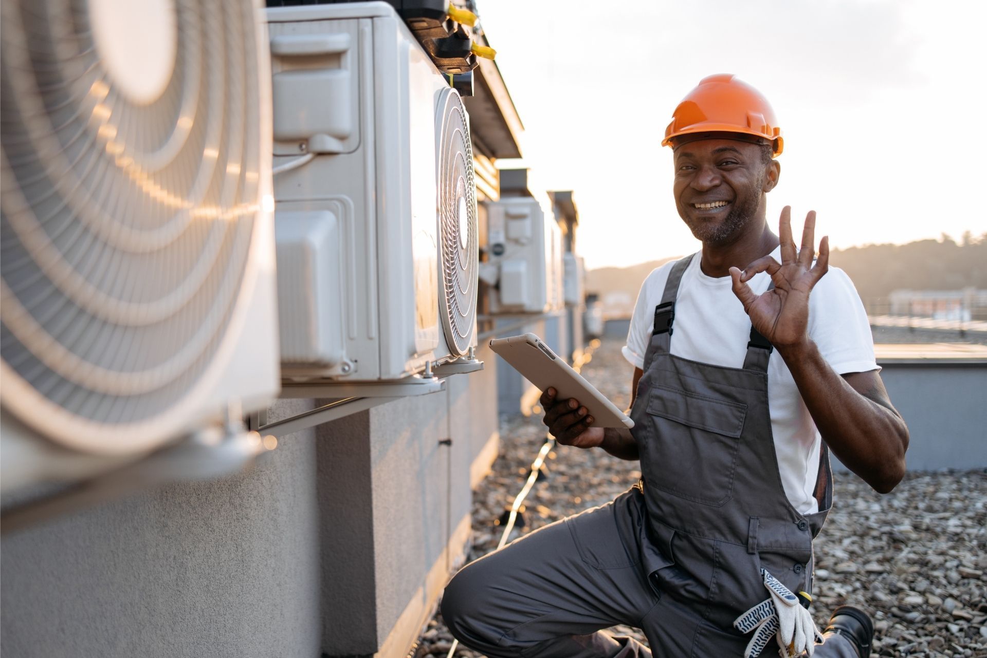 HVAC technician wearing mask and hard hat, working on AC units on a rooftop. HVAC technician wearing mask and hard hat, working on AC units on a rooftop.