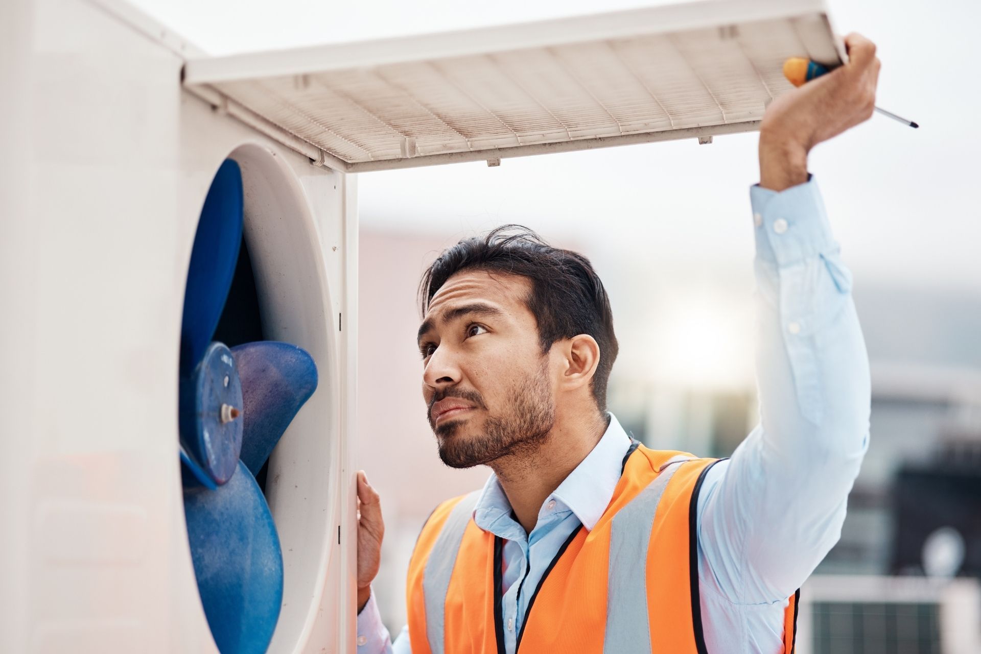 HVAC technician wearing mask and hard hat, working on AC units on a rooftop. HVAC technician wearing mask and hard hat, working on AC units on a rooftop.
