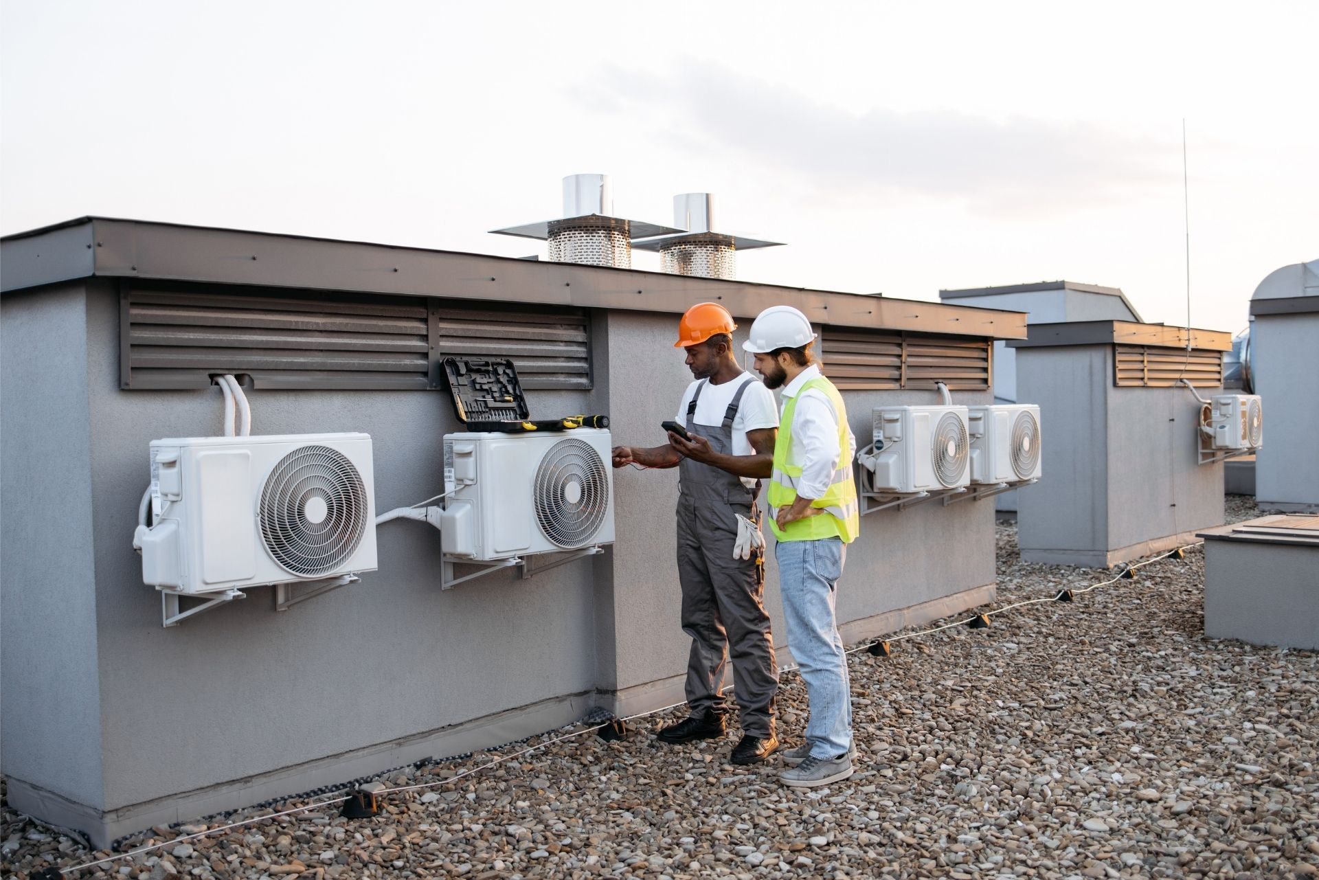 HVAC technician wearing mask and hard hat, working on AC units on a rooftop. HVAC technician wearing mask and hard hat, working on AC units on a rooftop.