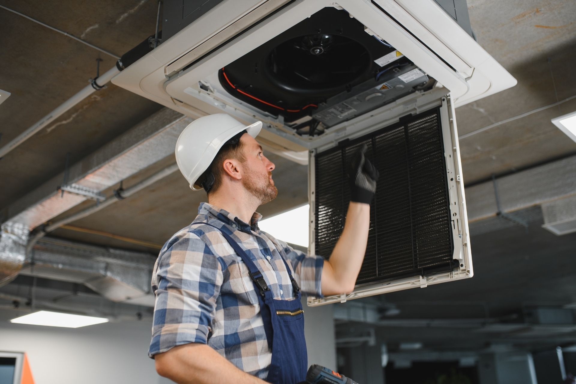 HVAC technician wearing mask and hard hat, working on AC units on a rooftop.