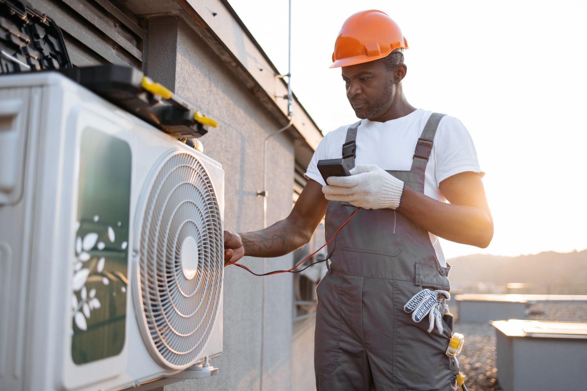 HVAC technician wearing mask and hard hat, working on AC units on a rooftop.