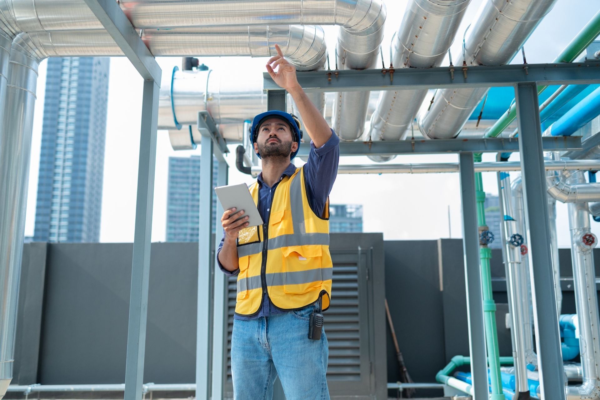 HVAC technician wearing mask and hard hat, working on AC units on a rooftop.