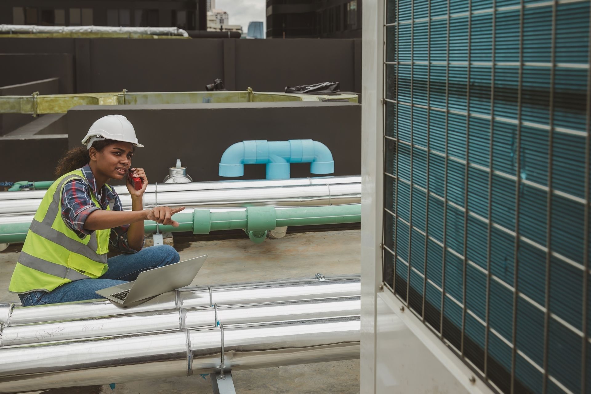 HVAC technician wearing mask and hard hat, working on AC units on a rooftop.