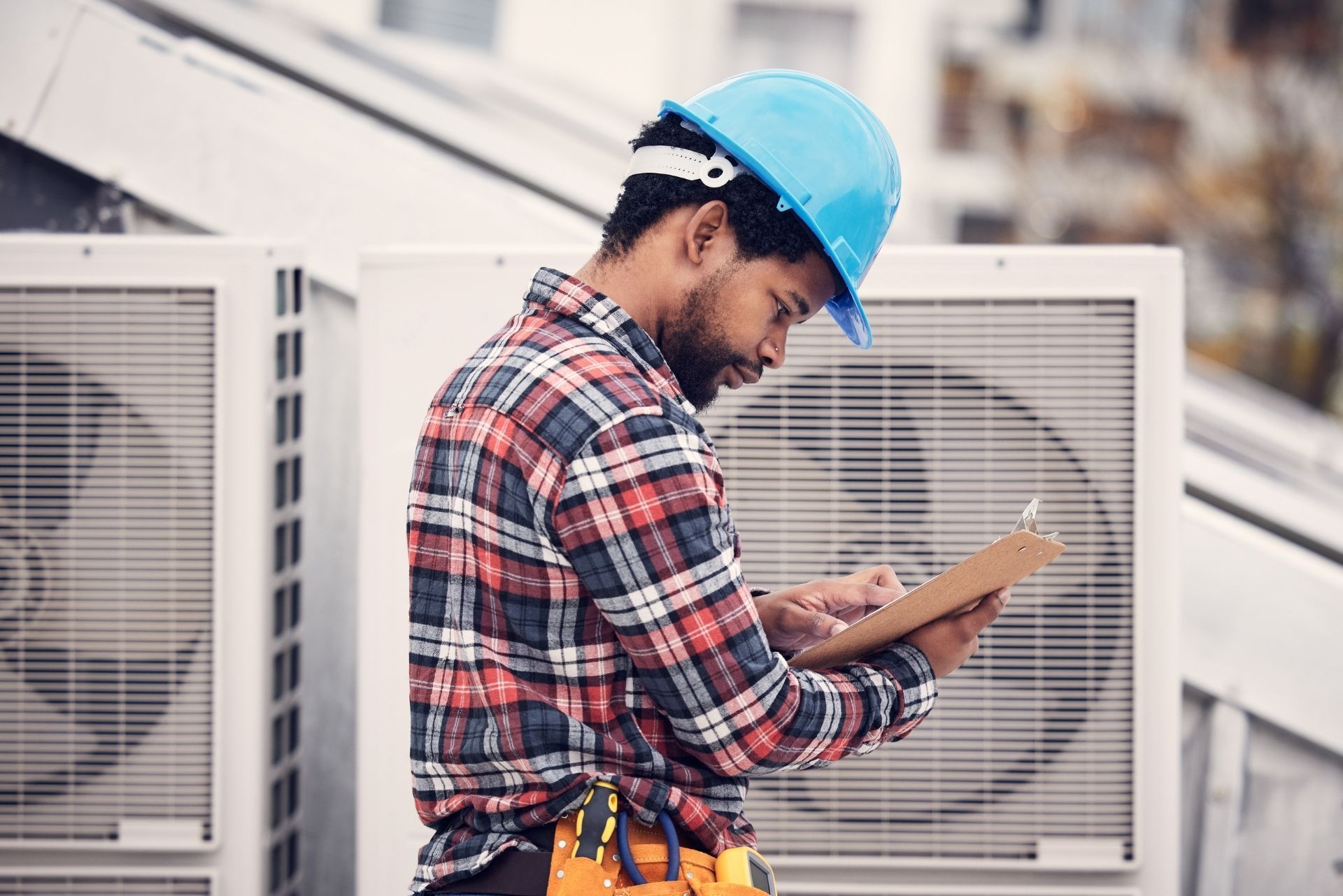 HVAC technician wearing mask and hard hat, working on AC units on a rooftop.