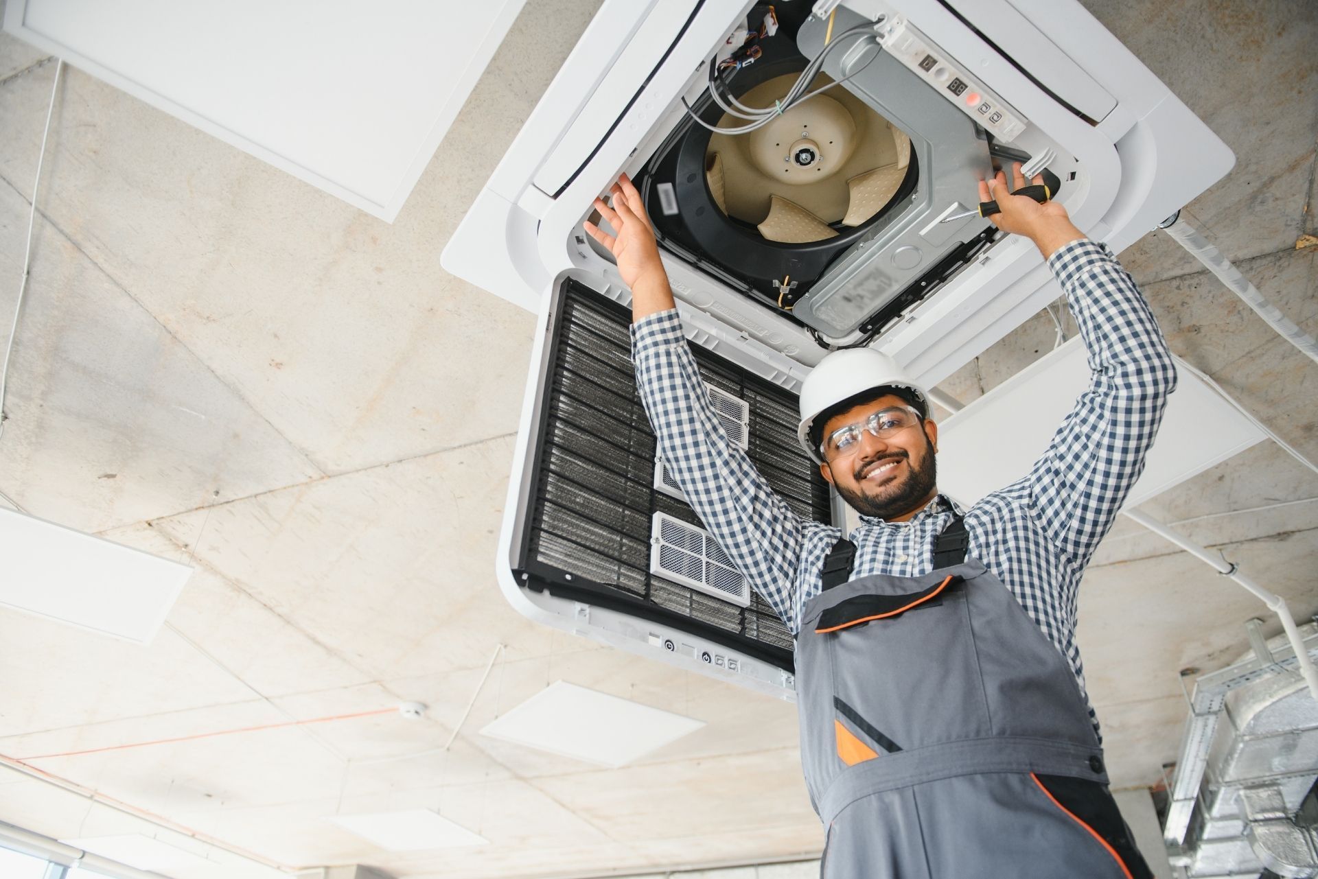HVAC technician wearing mask and hard hat, working on AC units on a rooftop. HVAC technician wearing mask and hard hat, working on AC units on a rooftop.