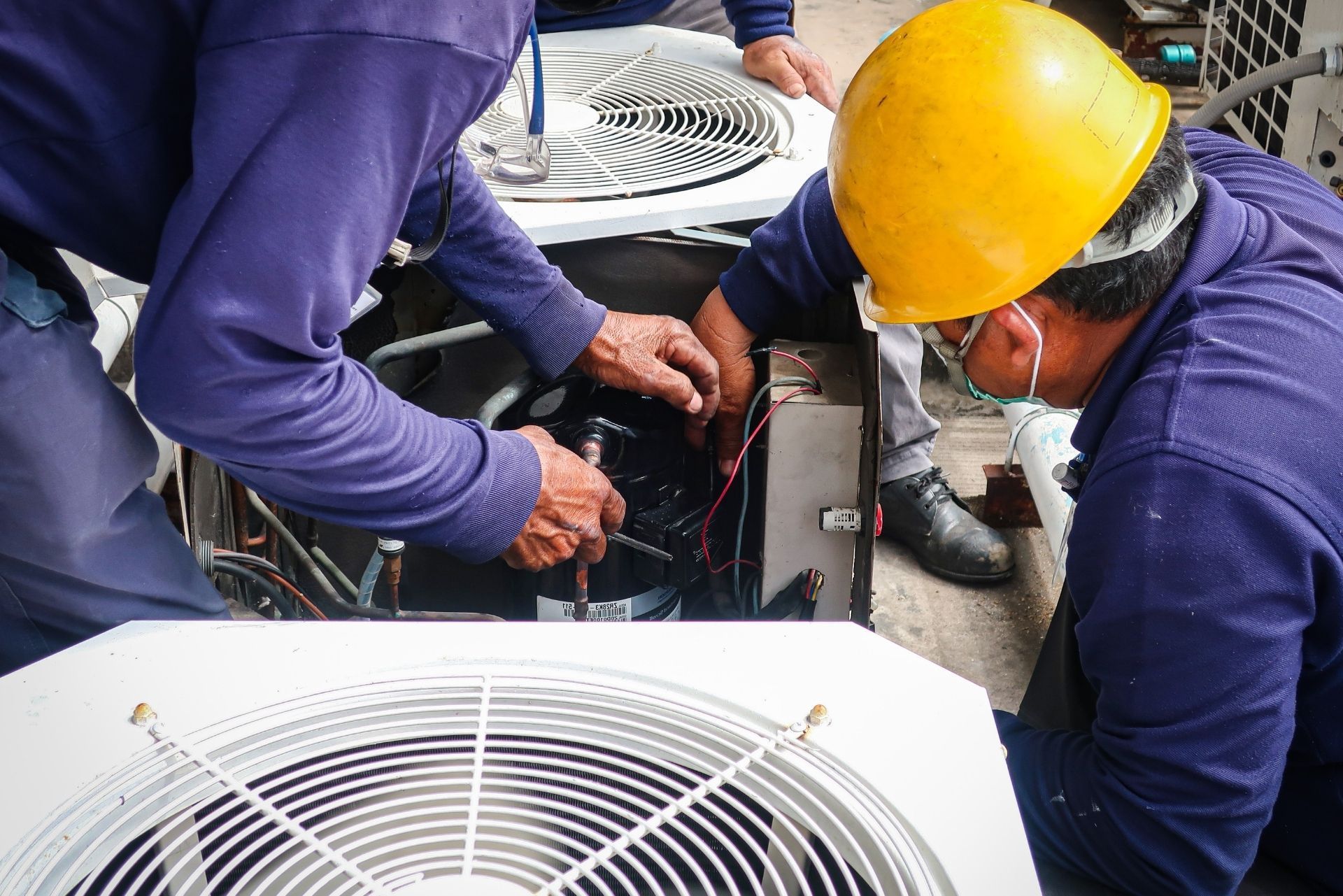 HVAC technician wearing mask and hard hat, working on AC units on a rooftop. HVAC technician wearing mask and hard hat, working on AC units on a rooftop.