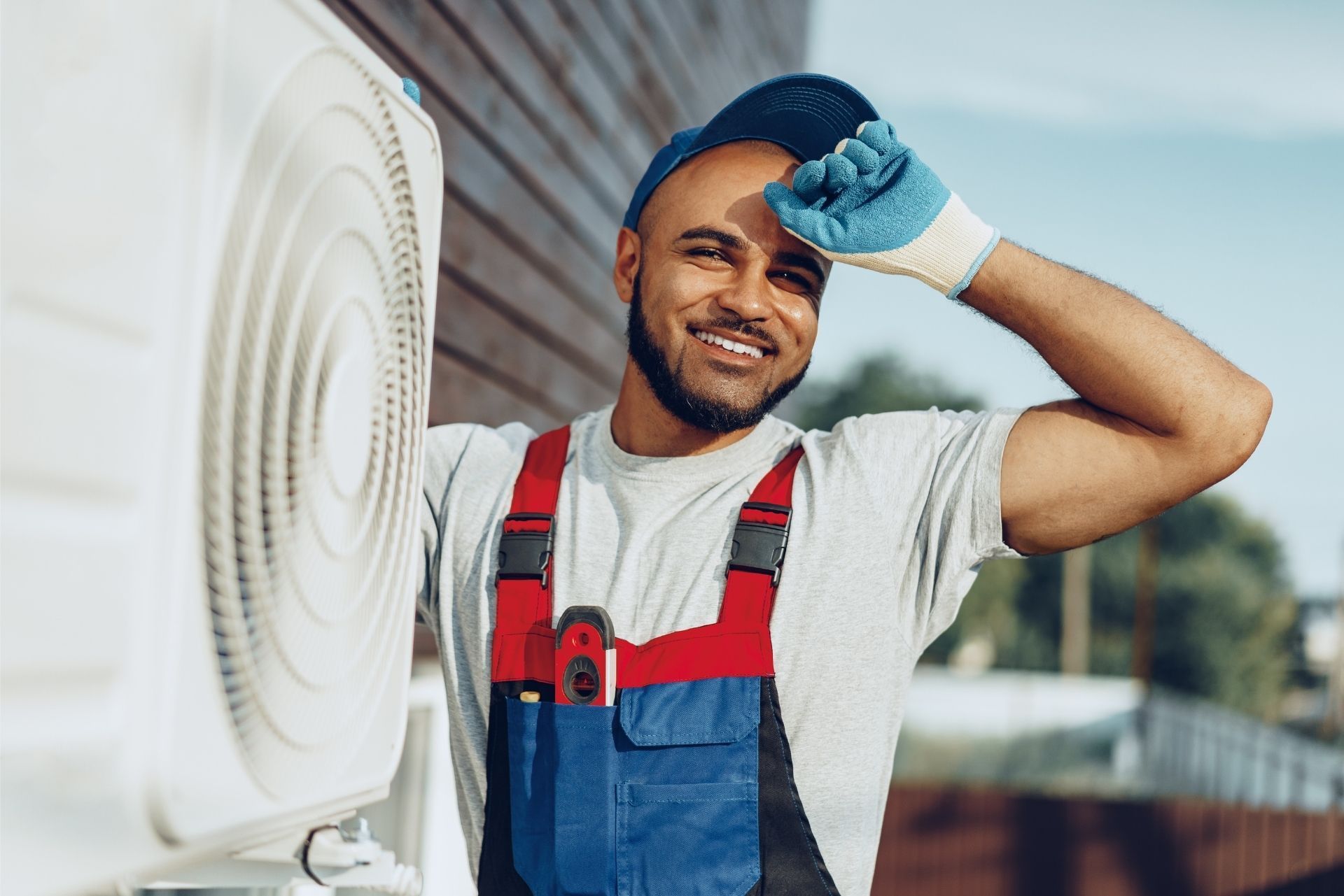 HVAC technician wearing mask and hard hat, working on AC units on a rooftop.
